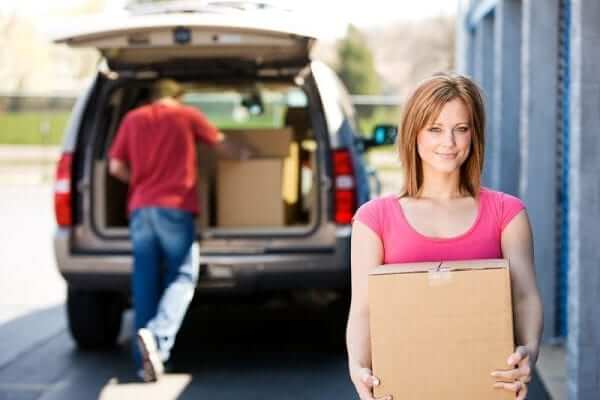 a woman carrying a cardboard box while her husband unloads the rest from the car