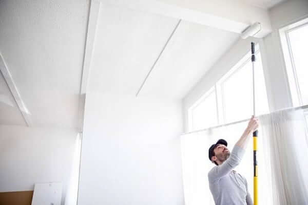 A man painting the cieling with a long paint roller