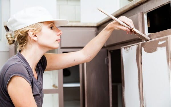 A woman painting the kitchen cabinets while sititng down on the floor